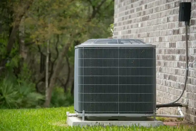 Outdoor central air conditioning unit installed next to a brick house, surrounded by green grass.