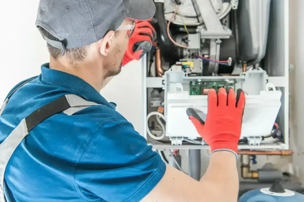 HVAC technician in red gloves and safety gear inspecting and preparing a Rheem furnace unit for installation, performing system diagnostics and setup.