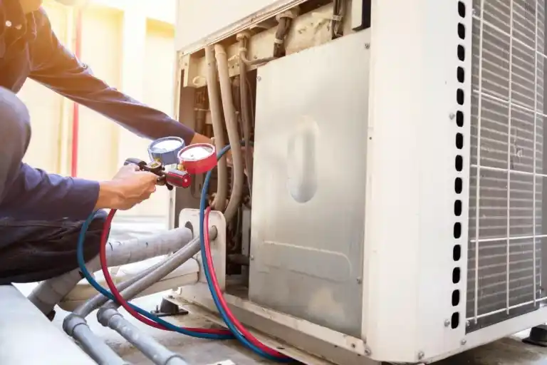 HVAC technician performing seasonal AC maintenance using pressure gauges on an outdoor air conditioning unit.