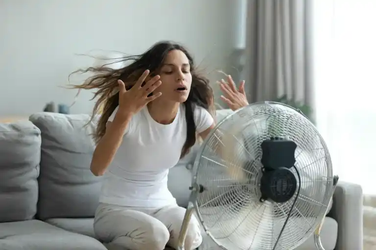 Frustrated woman cooling off in front of a fan at home due to a broken air conditioner.