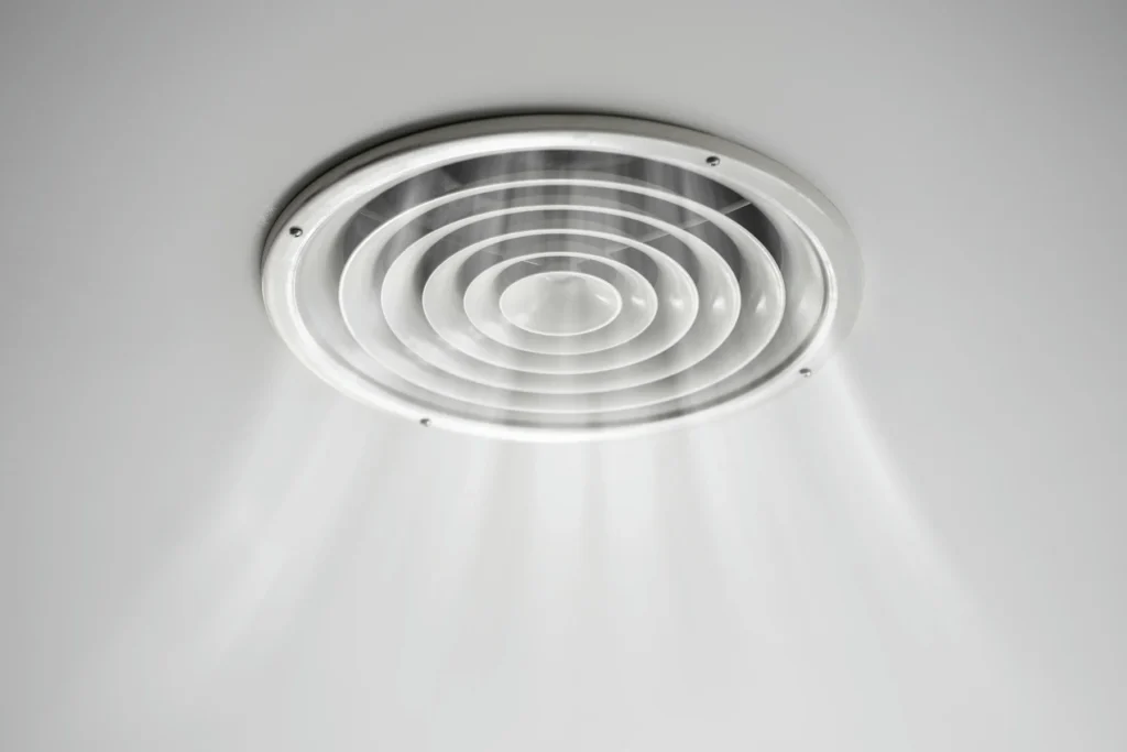Circular ceiling air vent dispersing cool air from an air conditioning system.